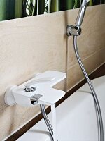 A white bath tap and a shower hose on a tiled wall