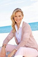 A young blonde woman wearing a white blouse and a dusty pink cardigan