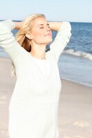 A young blonde woman on a beach wearing a pastel green jumper