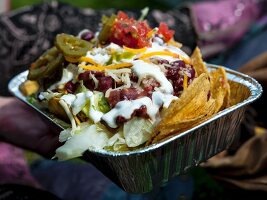 Nachos with salsa, pickled jalapenos and sour cream in an alumnium tray