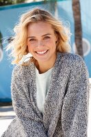 A young blonde woman in a white top and mottled grey knitted cardigan