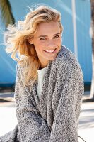 A young blonde woman in a white top and a grey mottled knitted cardigan