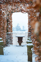 View of pergola, snow-covered garden and stone vase