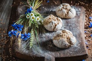 Gesunde Vollkornbrötchen mit Ähren und Feldblumen auf Holzbrett