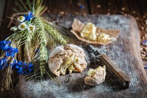 A healthy wholemeal bread roll with butter, ears of corn and field flowers on a wooden chopping board