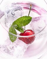 A glass of water with a cherry, ice cubes and mint