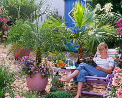 Palmenterrasse mit Holzliegestuhl, Frau liest Buch