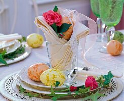 Pink (rose) in cloth napkin in glass on saucer with Easter eggs