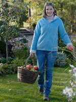 Junge Frau trägt einen Weidenkorb mit Äpfeln