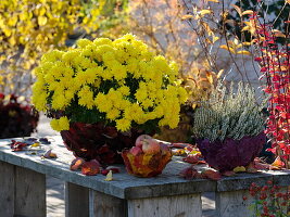 Autumn chrysanthemum, broom heather and apples in bowls covered with leaves