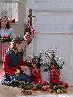 Mädchen neben roten Nikolausstiefeln, gefüllt mit Abies (Tanne), Äpfeln