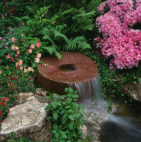 Wasserspiel: Mühlstein-Wasserfall, umgeben von Farnen, Rhododendron und Akeleien.