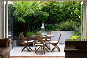 Kleiner Stadtgarten - Inside Out - Blick durch die Hintertür auf die Terrasse mit Hochbeeten, Dicksonia Antarctica und Tisch und Stühlen