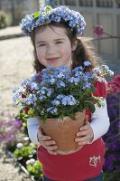 Mädchen mit Myosotis (Vergißmeinnicht) im Topf und als Kranz