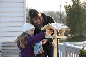 Mother and daughter filling a bird feeder