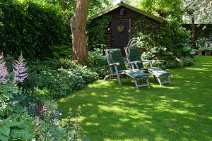 Loungers in the shade under a large tree, garden house, beds with shade perennials