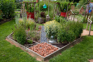 Herb bed with peppermint (Mentha piperita) and rue 'Variegata' (Ruta graveolens), glass bell, paths with slate pieces, broken bricks and tree slices