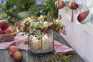 Glas-Windlicht im Drahtkorb mit Kranz aus Hydrangea (Hortensie) und Rosa