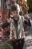 Girl with autumn necklace of purple string, physalis (lanterns), pink