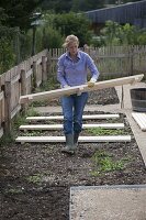 Frau legt Holzroste als Wege im gleichmäßigen Abstand in die Beete