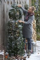 Woman adorns Christmas tree branches with twigs of Picea omorica