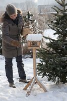 Frau füllt Vogelhaus mit Sonnenblumenkernen