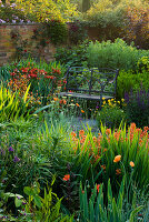 WOLLERTON Old HALL, SHROPSHIRE. A PLACE TO SIT. Metal SEAT AND VIEW ACROSS LANHYDROCK Garden with CROCOSMIA 'CONSTANCE' AND ERYSIMUM 'Apricot DELIGHT' IN FOREGROUND.