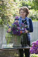 Frau steckt Strauß aus Allium 'Globemaster' (Zierlauch), rosa (Rosen)