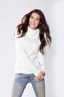 A brunette woman wearing a white cable-knit jumper and jeans