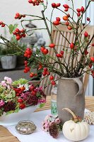 Branches of rose hips in stoneware jar next to autumnal flowers