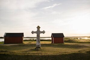 The stone cross of Kapelludden with wooden huts in the background on the island of Öland in southern Sweden