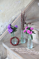Asters and autumn grasses in small glass bottles and circlet of rose hips decorating stair tread