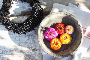 Wreath of dogwood berries next to zinnia flowers in bowl of water