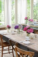 Gedeckter Tisch mit mehreren Hortensiensträußen im Wintergarten