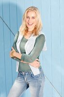 Blonde Frau in grünem Strick-Shirt, grauem Pullover über den Schultern und Jeans