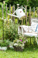 Sitzplatz am Staketenzaun mit Gießkanne und Wildblumenstrauß