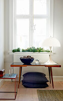 Designer lamp on retro table in front of window with conifer branches on sill