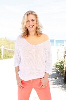 A blonde woman wearing an orange top, a white knitted jumper and orange trousers on the beach