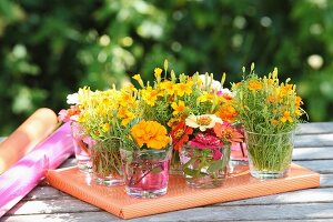 Many posies of garden flowers in drinking glasses arranged on top of wrapped gift
