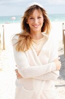 A blonde woman wearing a cream jumper and a white hooded cardigan on the beach