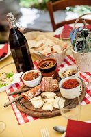 Holzteller mit Antipasti (Wurst, Käse, Oliven, in Öl eingelegte Pilze und getrocknete Tomaten), Rotwein und Brotkorb auf Tisch in Taverne