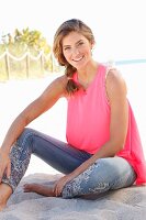 A young woman wearing a pink top and jeans with flower embroidery on the beach