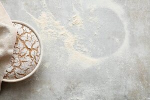 Baked bread in a round baking tin on a flour-dusted worktop