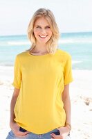 Blonde Frau in gelbem T-Shirt und Jeans am Strand