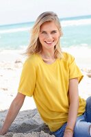 Blonde Frau in gelbem T-Shirt und Jeans am Strand