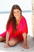 A brunette woman wearing a pink tunic on the beach