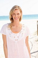 A blonde woman wearing a white embroidered T-shirt on the beach