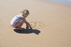 A little girl drawing a smiley face in the sand