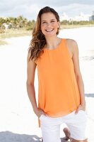 A young woman wearing an orange top and white trousers on the beach