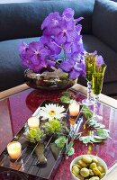 Arrangement of artificial flowers, bowl of water and tealights on coffee table